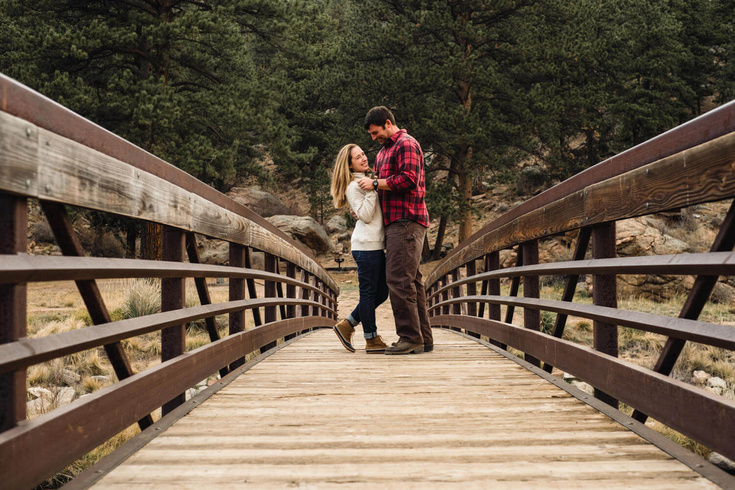 engaged couple standing, giggling on bridge