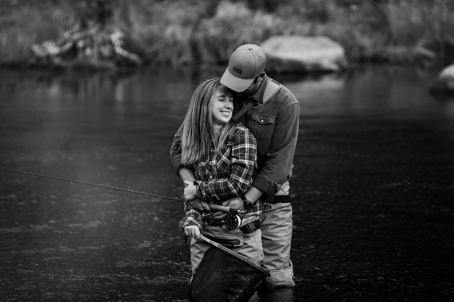 Black and white image of couple embracing while fishing in river.