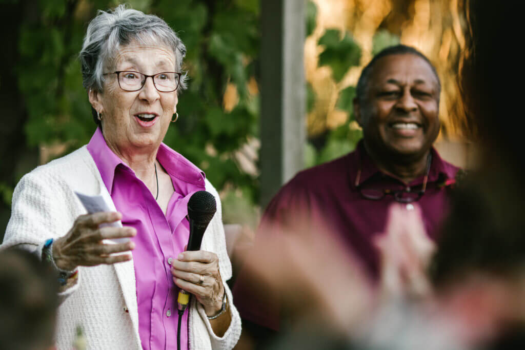 Multi racial couple gives toast at backyard anniversary celebration.