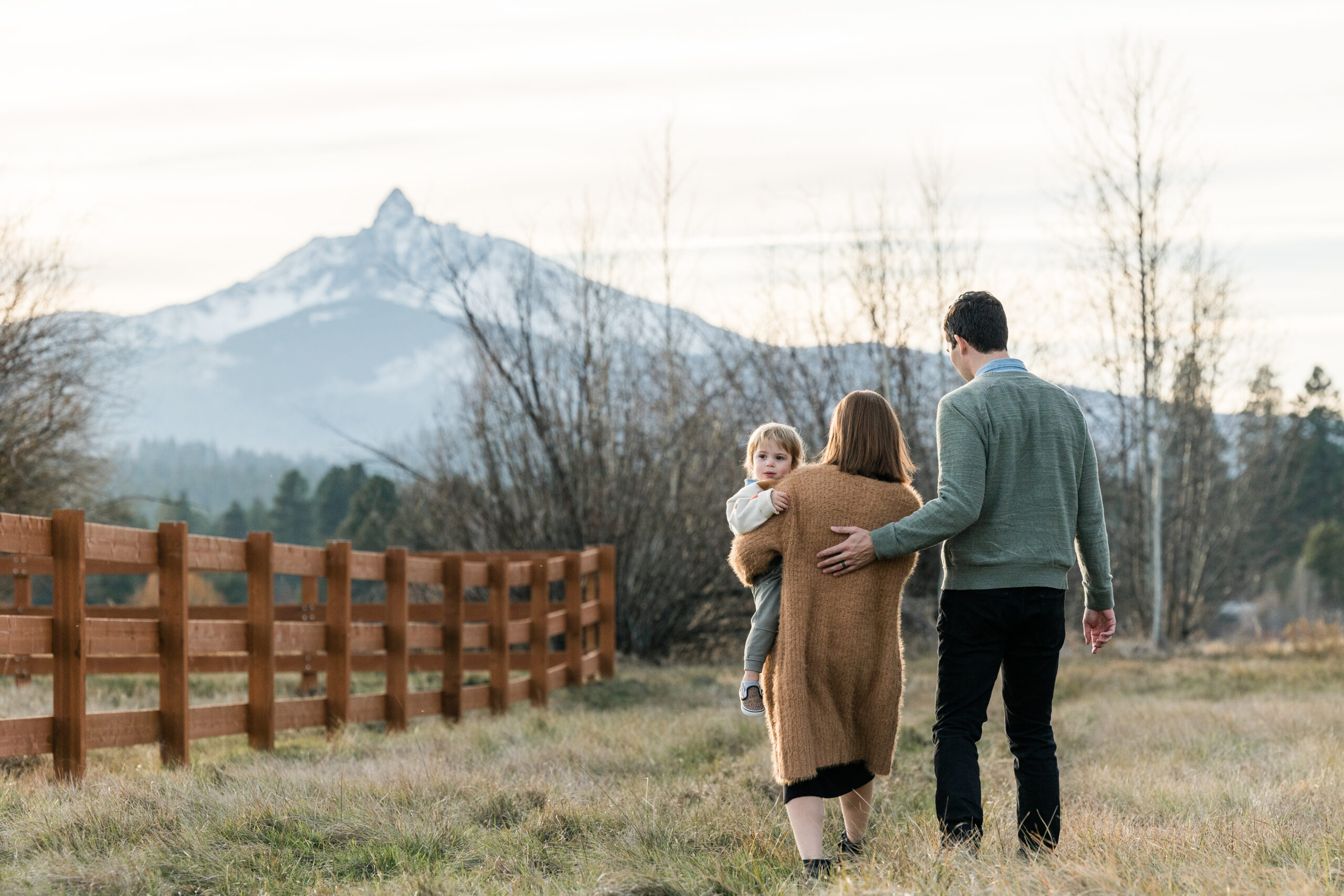 A family of three walk away from the camera towards one of the mountains at Black Butte Ranch.