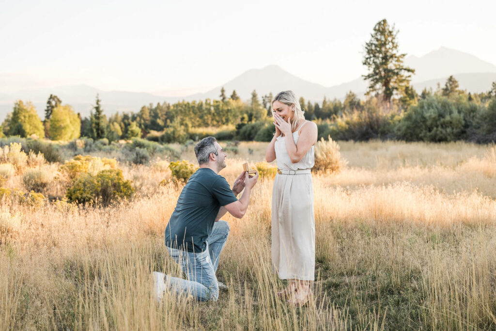 Man on his knee proposing to woman in a beautiful field.