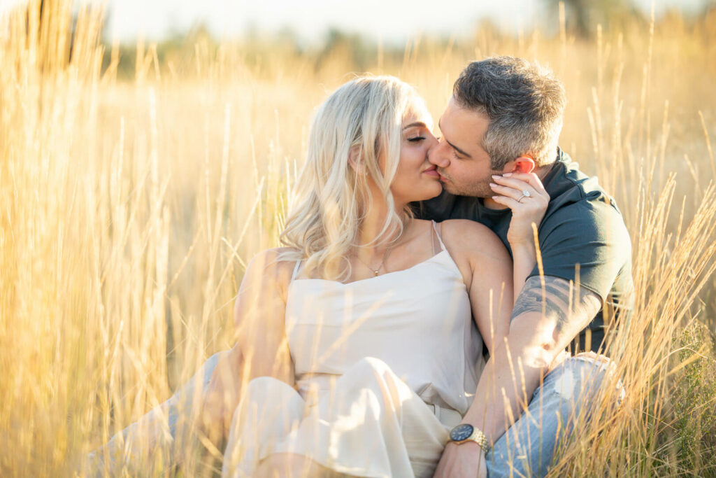 Couple seated in golden grass kissing.