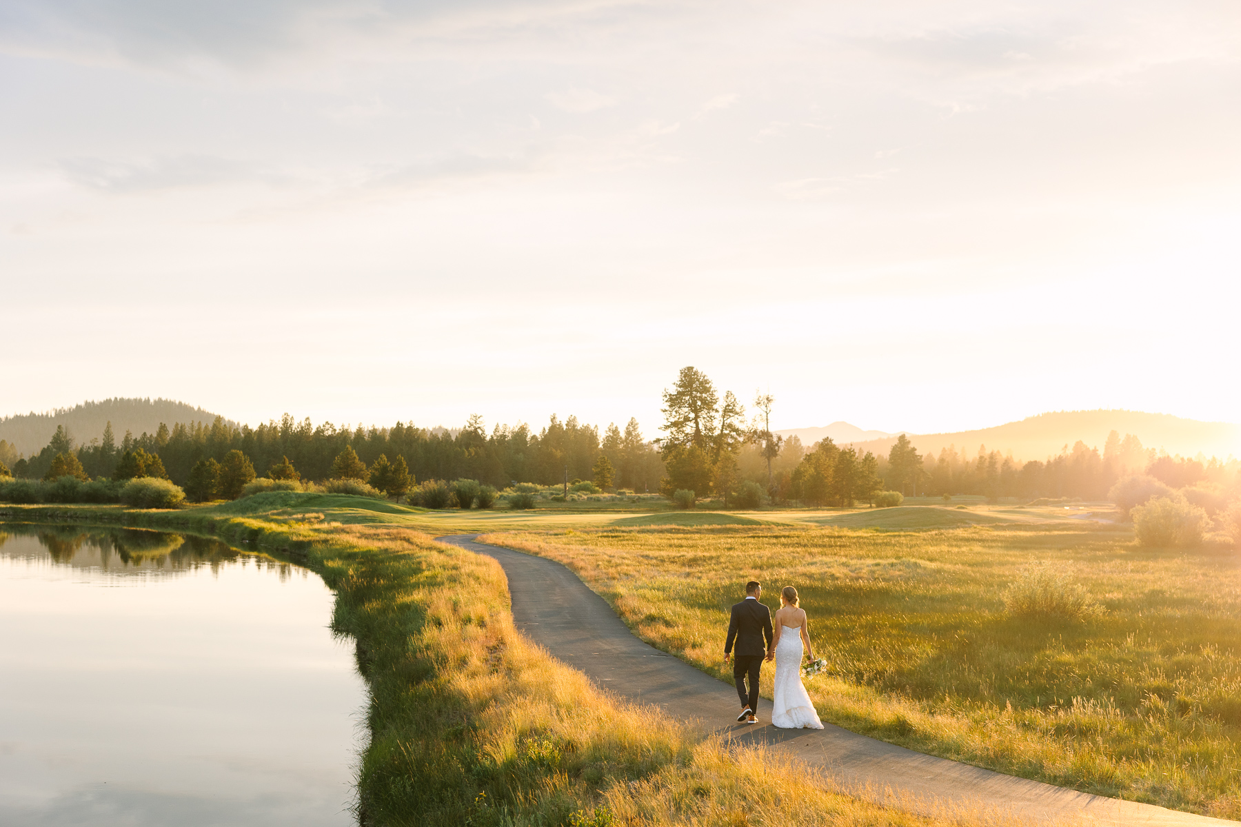 Couple walks on trail by the river as the golden setting sun illuminates the golf course.