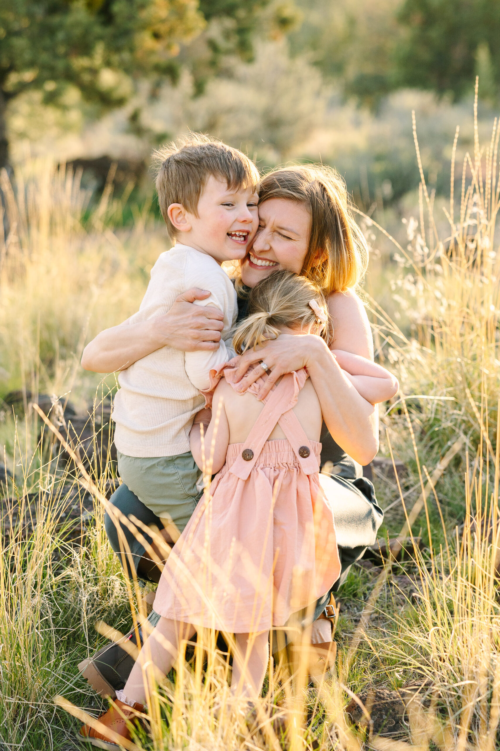 Young mother crouches down in the field while her two young kids squeeze and hug her.