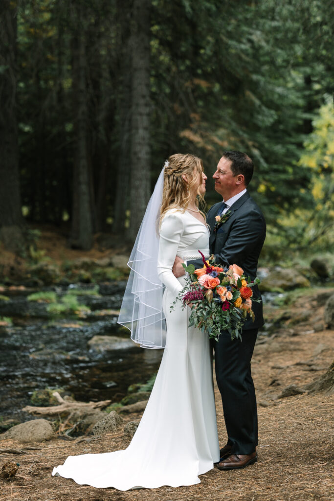 Full length portrait of the bride and groom in a wooden area near a creek. 