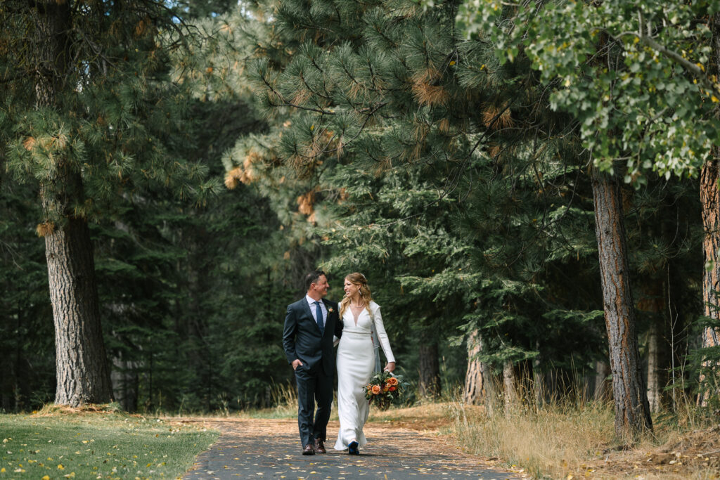 Bride and groom walk smiling at each other down a bike path in Black Butte Ranch. 