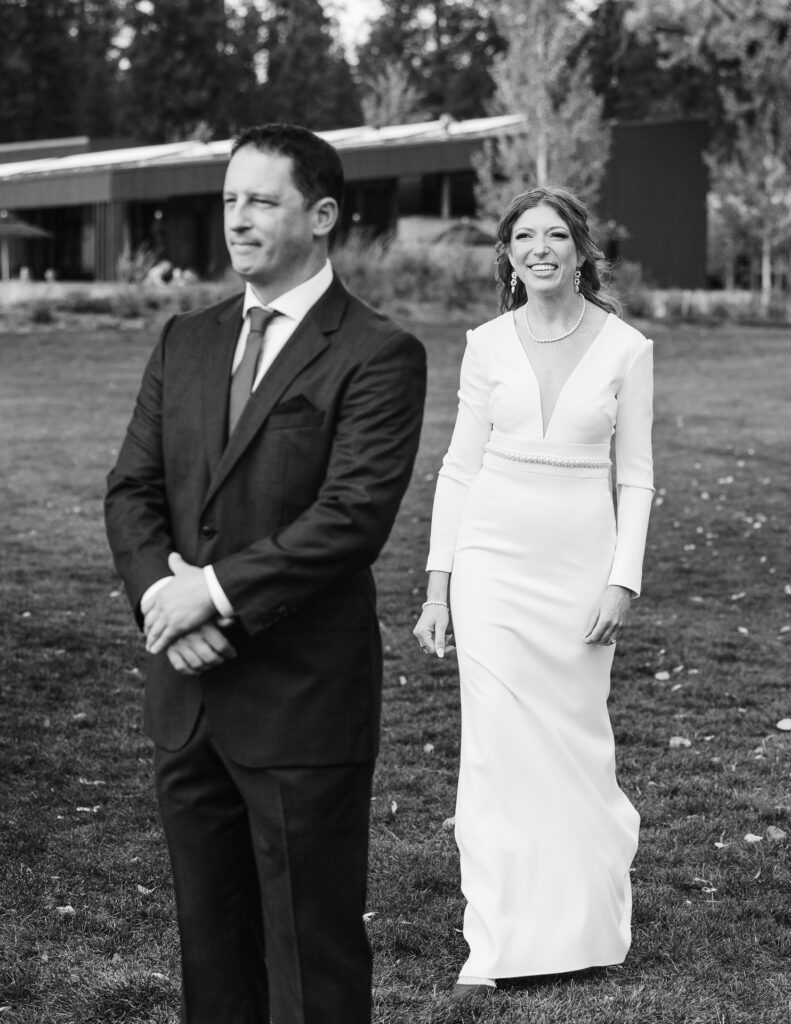 Smiling bride walks towards groom for their first look. Black and white image.