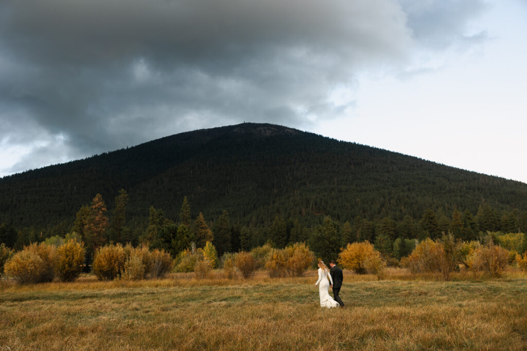 Couple walks away from the camera with Black Butte and golden shrubs in the distance.