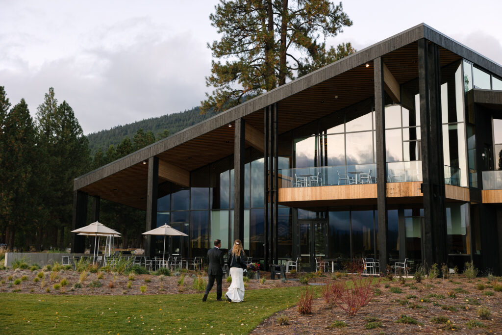 Bride and groom walk away from the camera towards the newly constructed Lodge at Black Butte Ranch. 