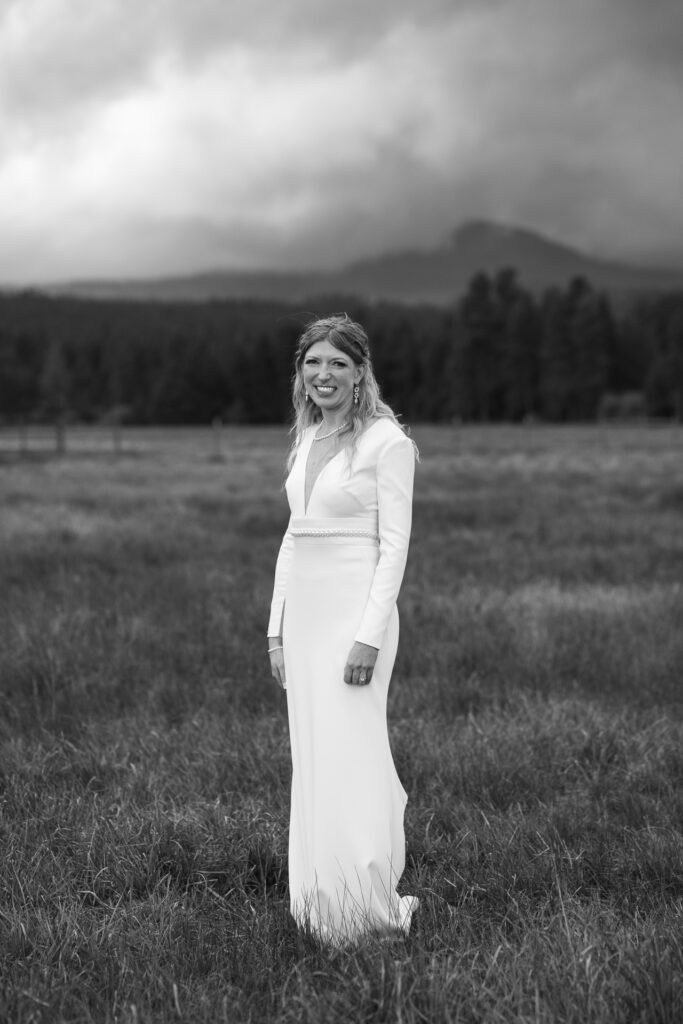 Full length moody black and white portrait of stunning bride in long sleeved, sleek wedding dress. 
