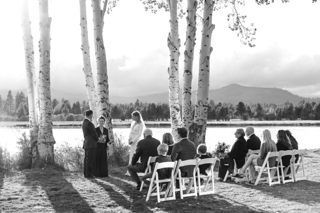 Black and white image, mountains in the distance are covered by clouds as the couple says "I do" near the aspen grove. 