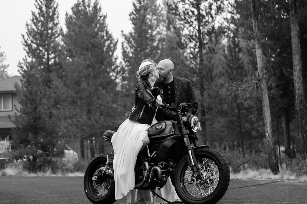 Bride sits on a Ducati while kissing her husband. Black and white photo.