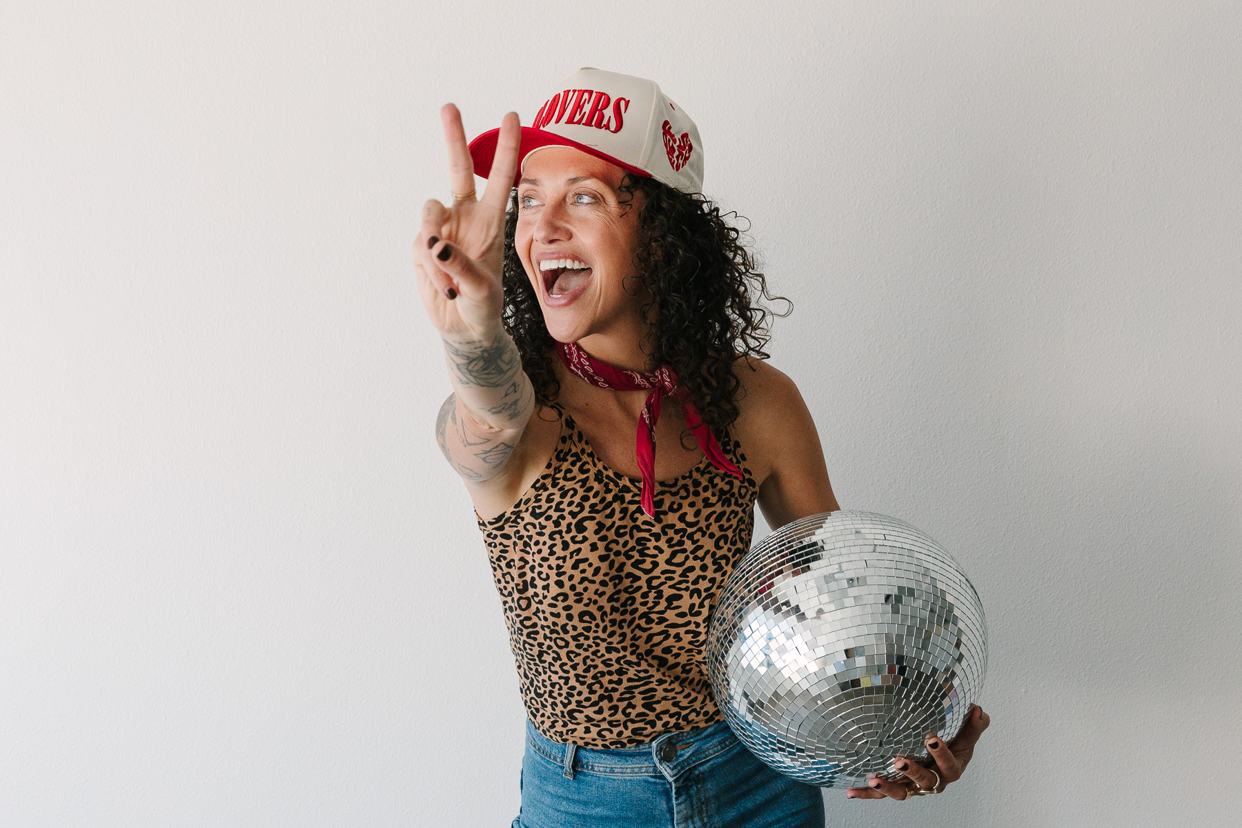 Woman holding disco ball with giant smile and holding out peace sign.