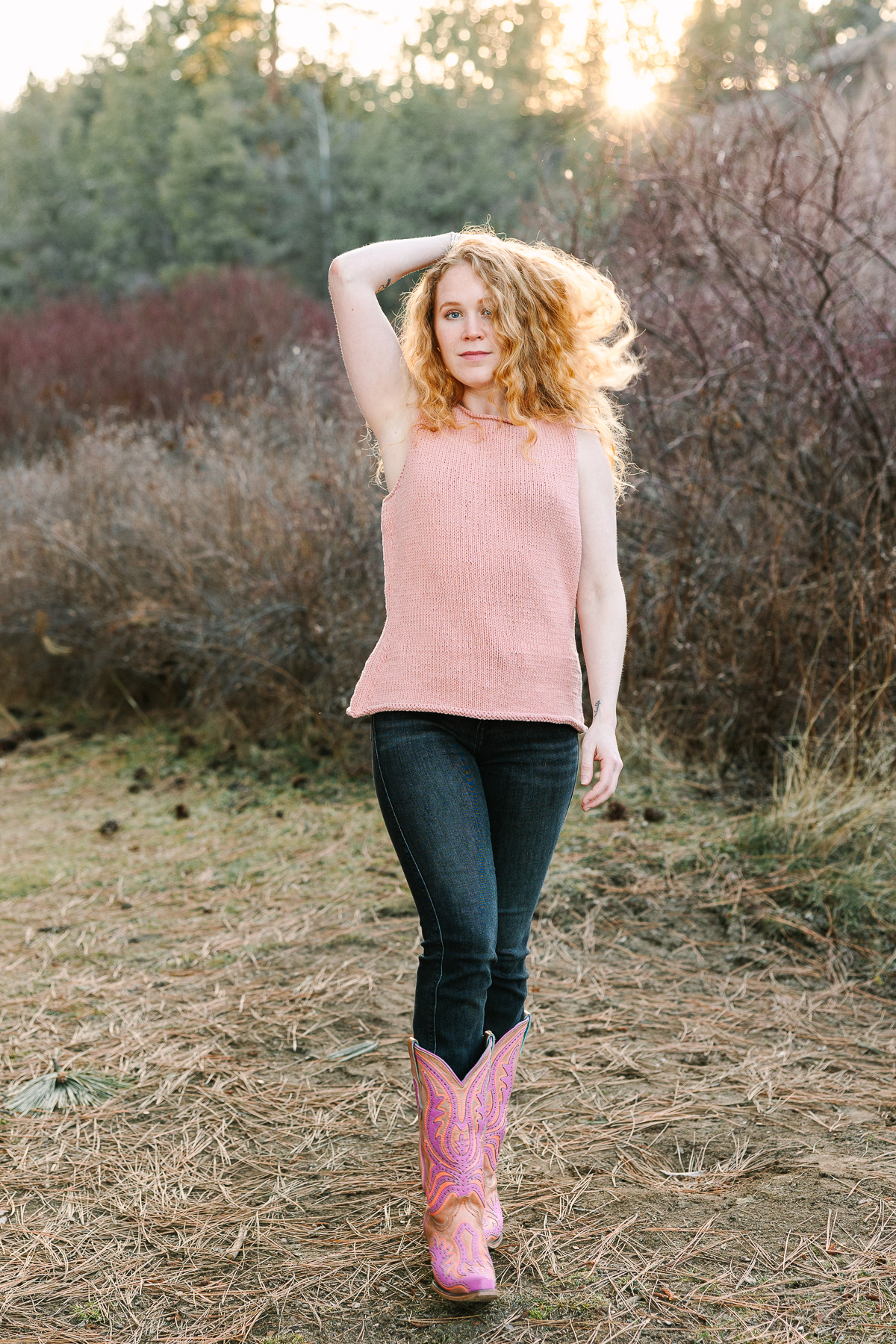 Girl with red hair, pink cowboy boots and a pink knit sleeveless sweater.