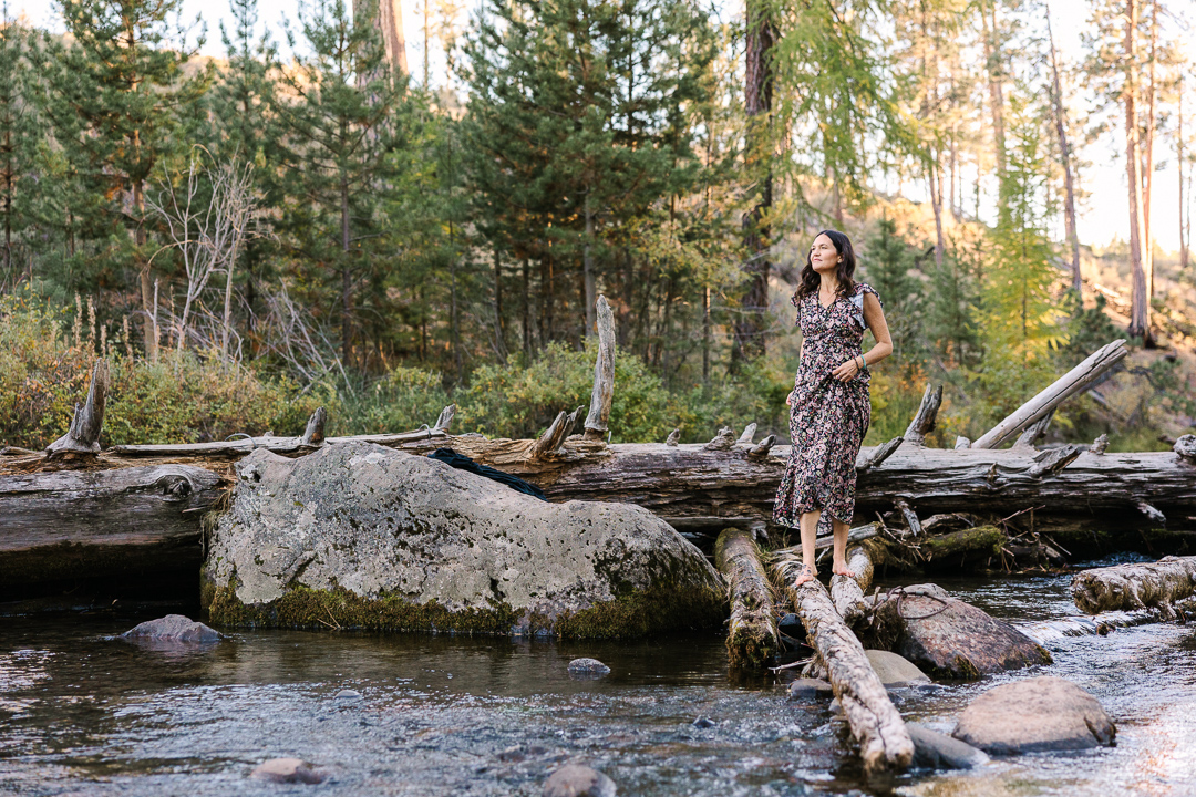 Women walks on fallen tree branch in river.