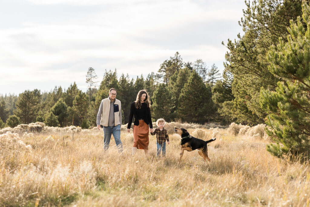 Young family plays with their dog in a meadow at Sunriver Resort.