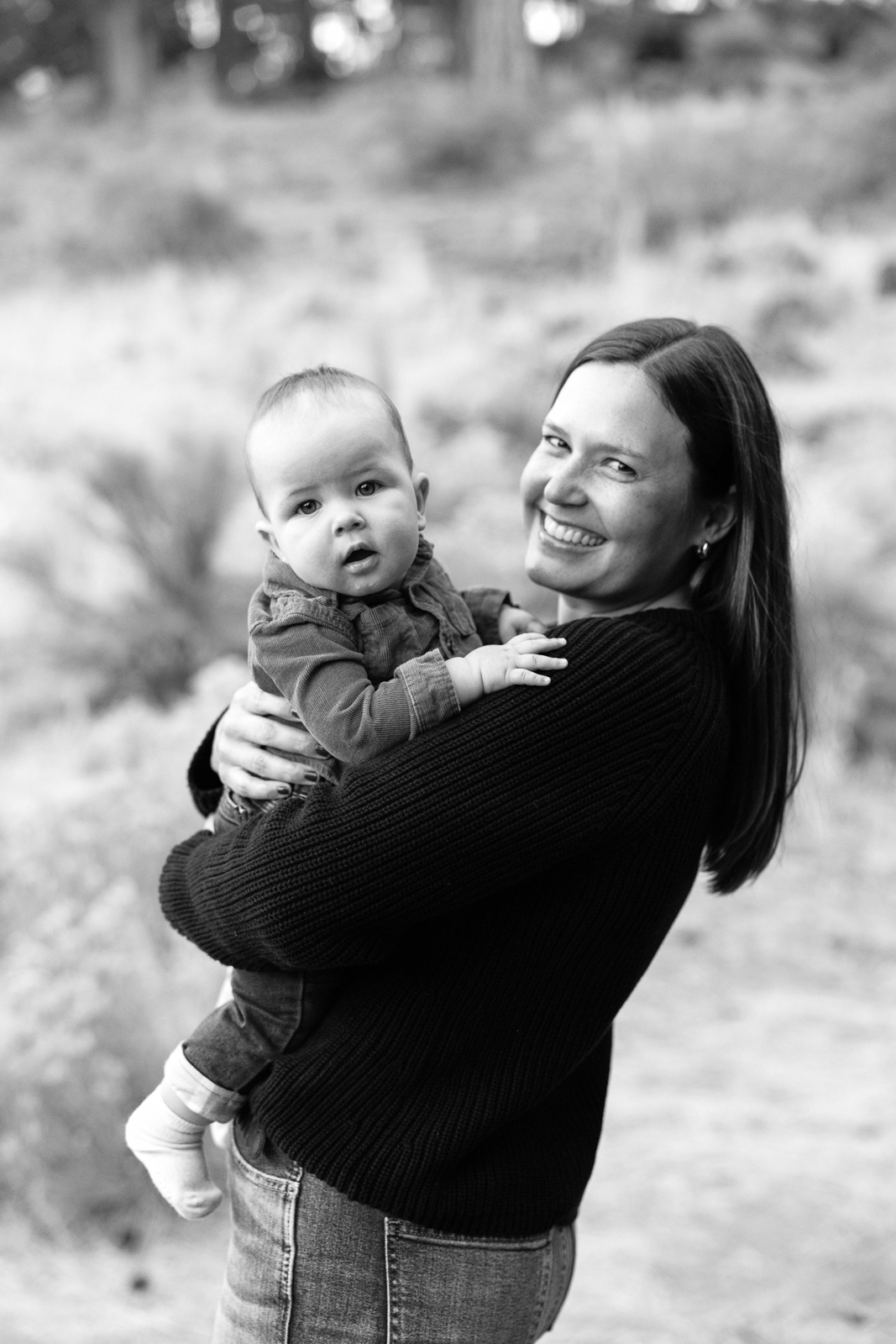 New mom and baby boy smile at the camera. Black and white image.