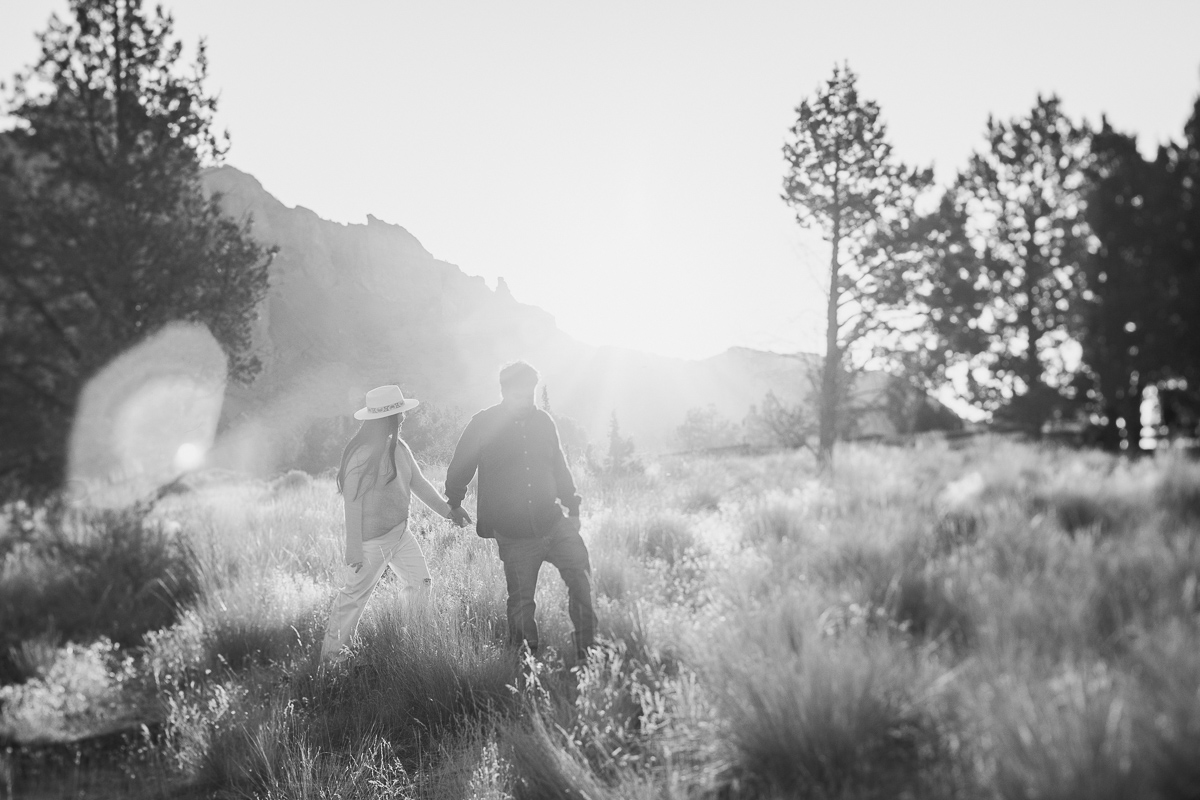 couple walks through a field. Black and white image that has a dreamy feel.