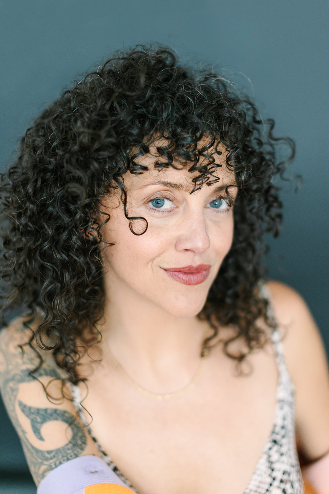 Portrait of a curly haired brunette against a grey backdrop.