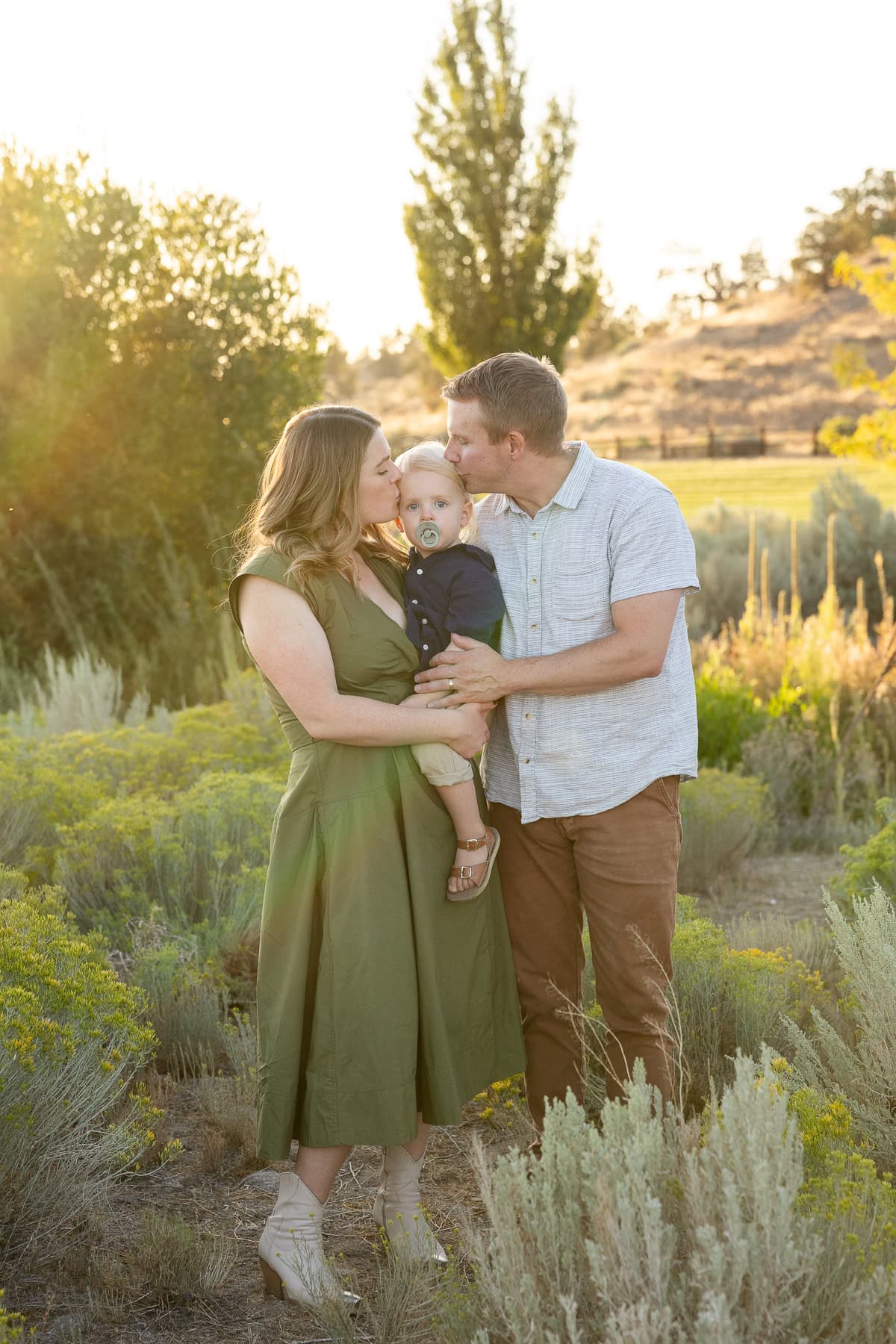 Mom and Dad kiss toddler on his cheeks as they pose for a photo.