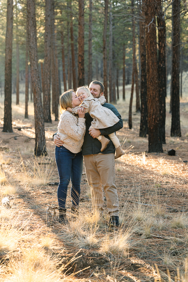 Dad holds young daughter and mom leans in and kisses her.