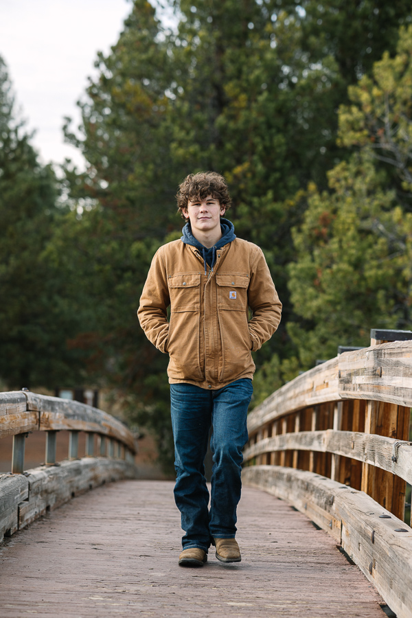 Senior boy walks towards the camera wearing denim jeans, blue hoodie and carhartt jacket.