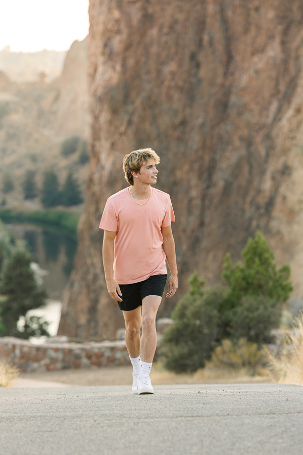 High school senior boy walks up path with enormous rocks in the background at Smith Rock State Park.