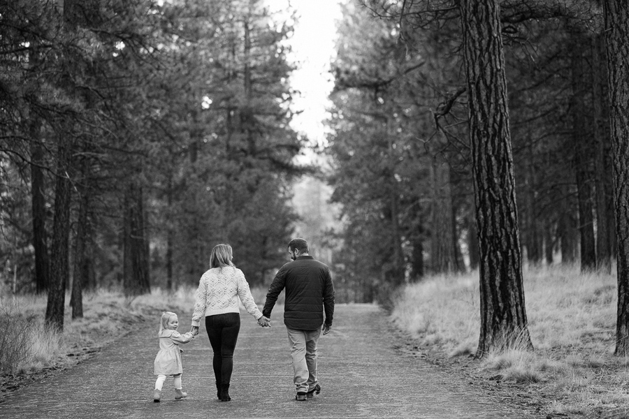 Black and white image of a family of three holding hands walking down a paved path at Shevlin Park in Bend.