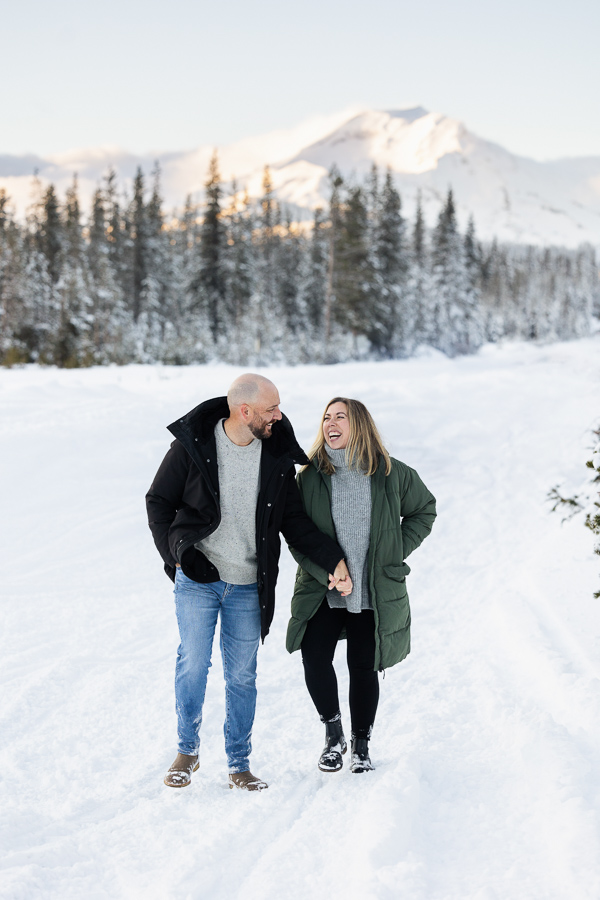 A couple in love holds hands and walks in the snowy landscape with mountains in the background.