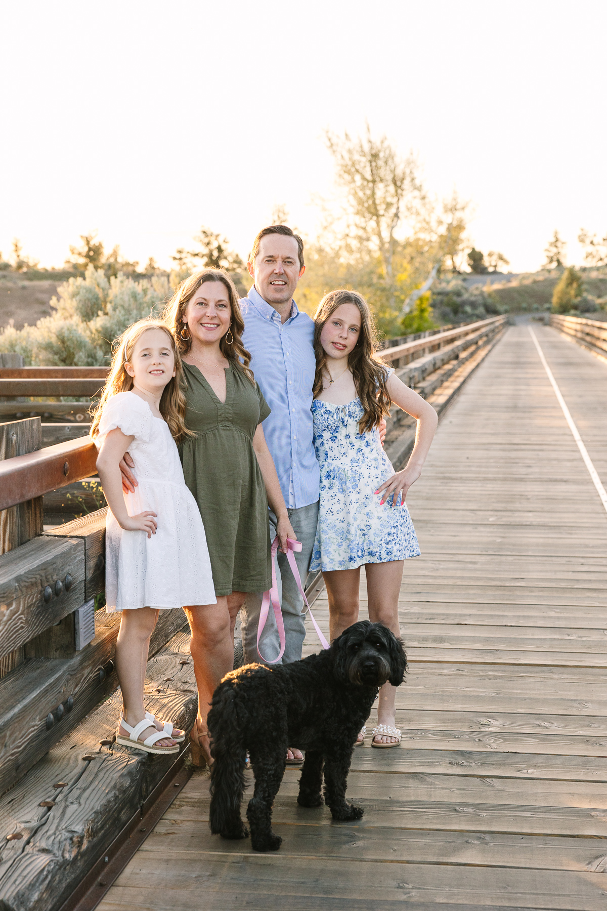 A family of four with their little black dog is photographed at Golden Hour on the trestle bridge at Brasada Ranch.