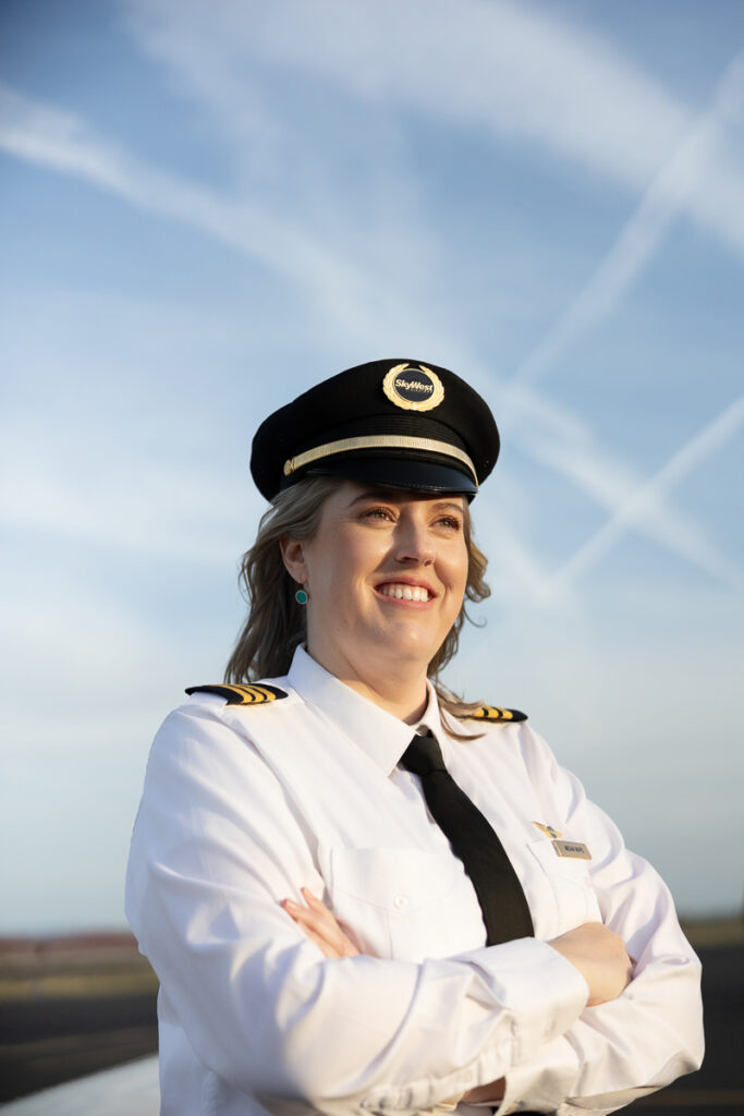 Female pilot stands confidently outside with the sky behind her.